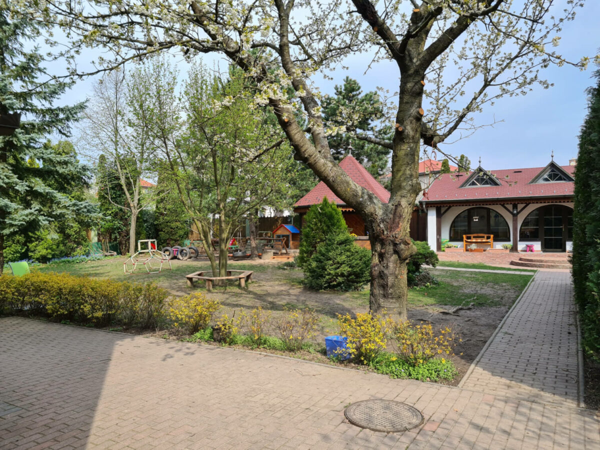 Celkový pohľad na záhradu Zahrajda - záhradný domček, stromy, lavička okolo stromu, záhradný altánok, detská preliezačka